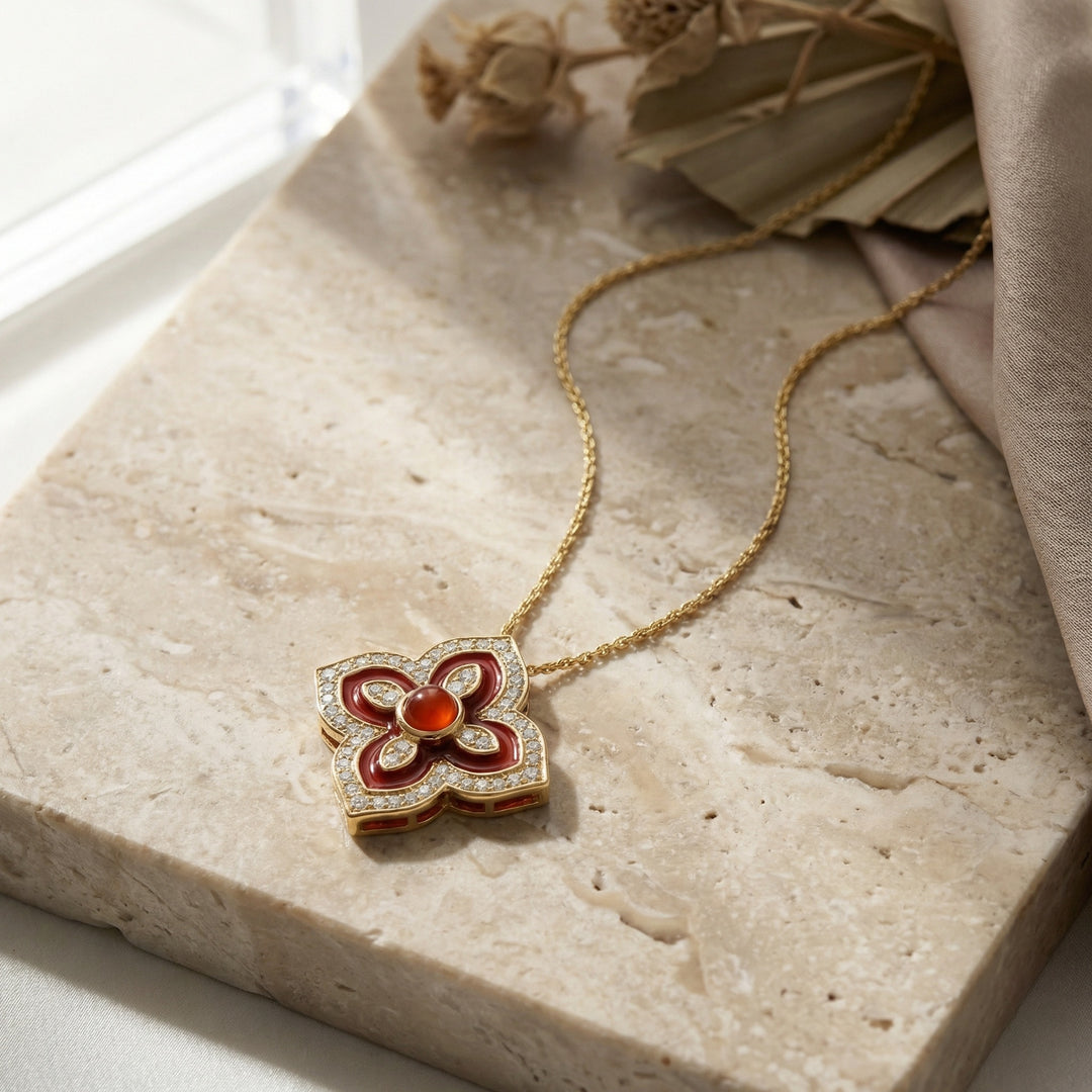 Gold necklace with a red and gold pendant on a stone surface