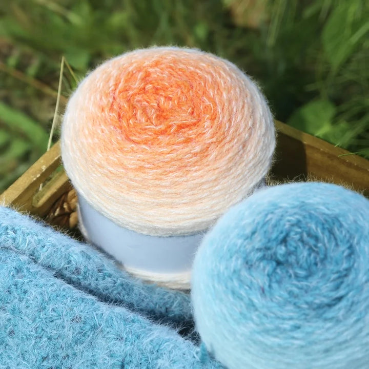 Two balls of yarn, one orange and white, the other blue, on a wooden surface with a blurred green background.