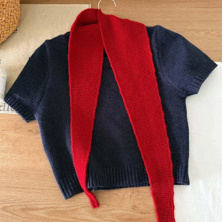 Navy sweater with a red scarf draped over it on a wooden surface.