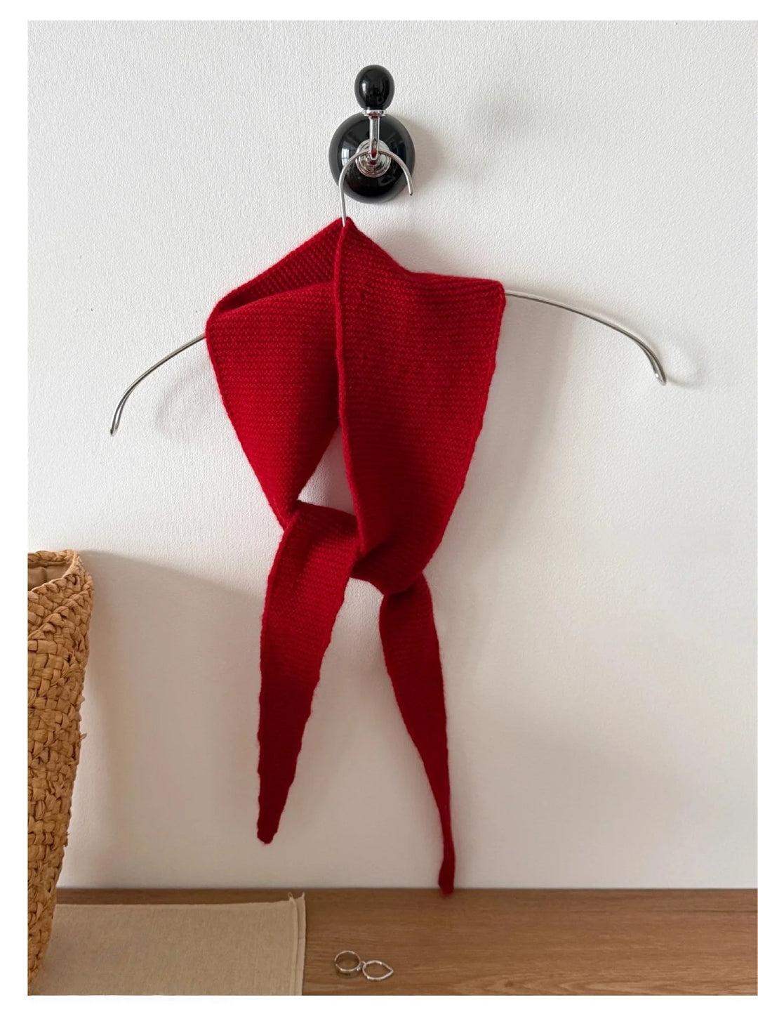Red knitted garment on a hanger against a white wall.