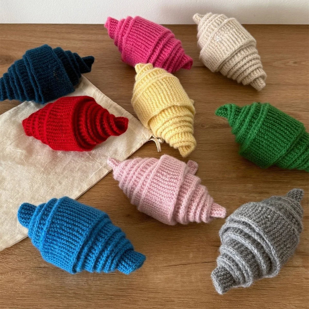 Colorful knitted toys shaped like croissants on a wooden surface