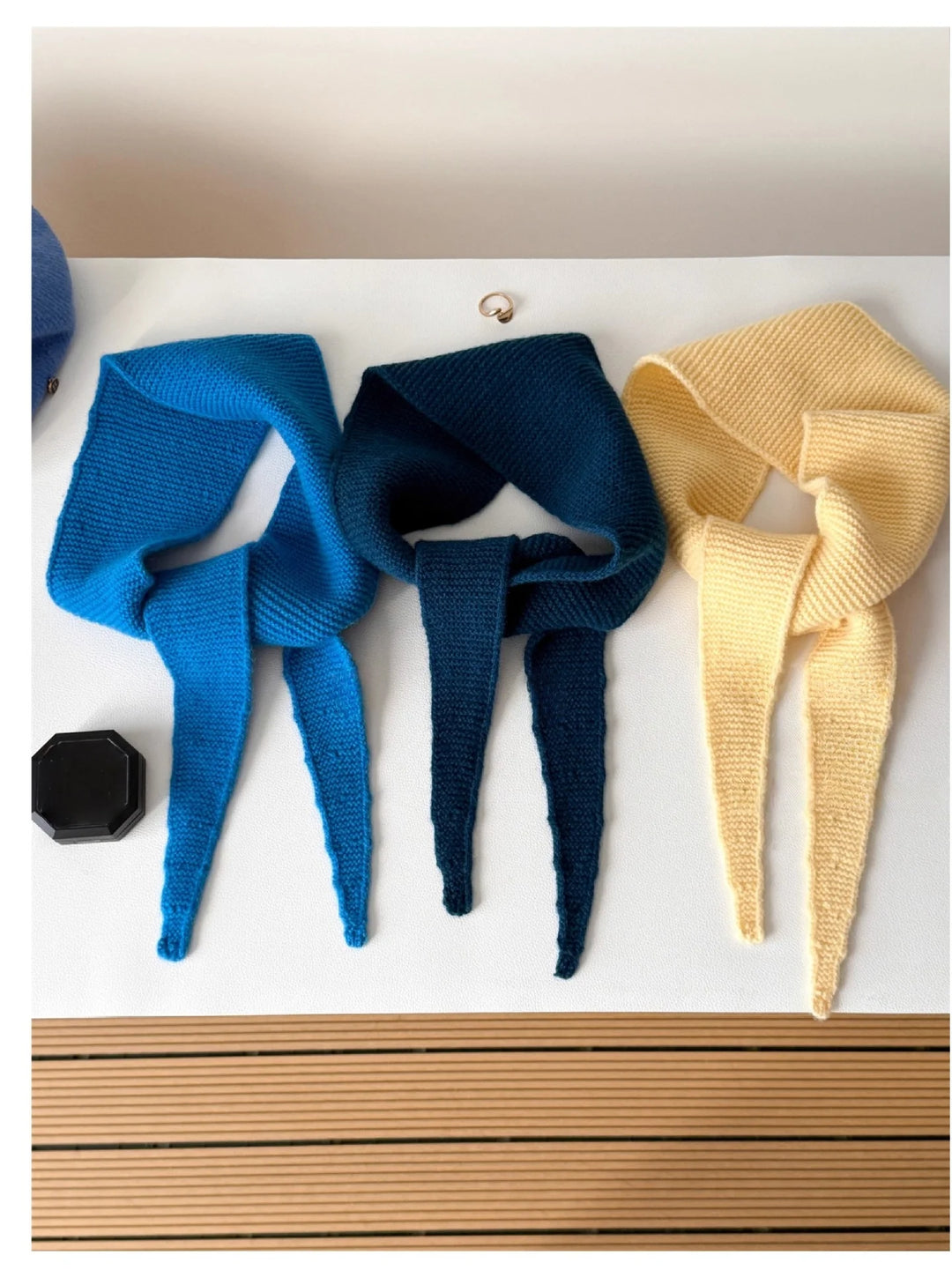 Three knitted headbands in blue, navy, and beige on a white surface.