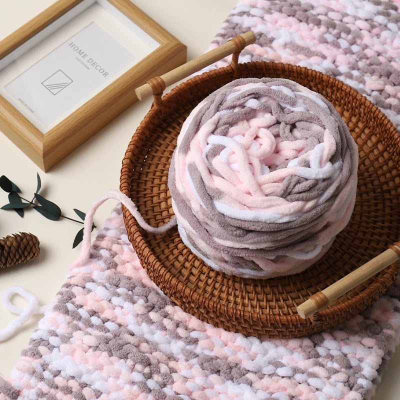 Ball of yarn with knitting needles on a woven tray, surrounded by knitted fabric and a framed picture.