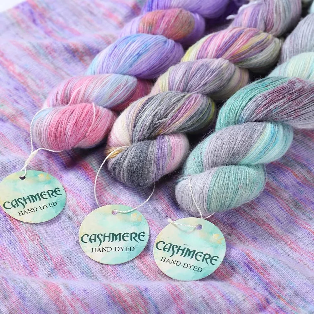 Colorful cashmere yarn skeins with 'hand-dyed' tags on a textured fabric background