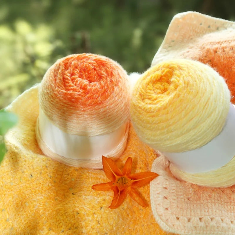 Three skeins of yarn in orange, yellow, and white with a small orange flower on a blurred green background.
